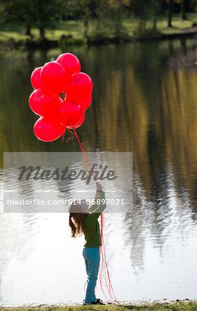 Young girl in front of lake with bunch of red balloons