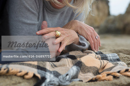 Mature couple lying on beach holding hands, close-up