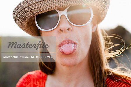 Mature woman wearing sunglasses and sunhat sticking out tongue Mature woman wearing sunglasses and sunhat sticking out tongue