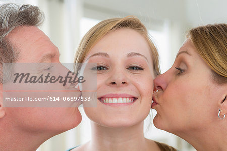 Mother and father kissing teenage daughter on cheek