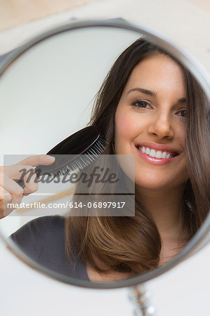 Young woman brushing hair in mirror