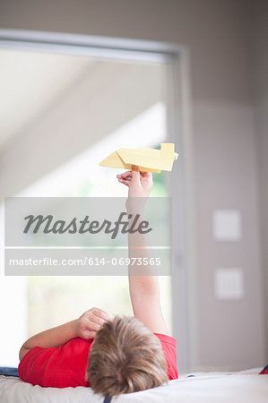 Boy on bed playing with paper aeroplane