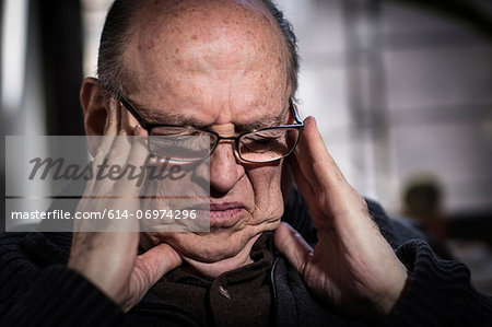 Senior man with eyes closed, wearing glasses, looking stressed