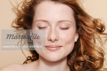 Studio shot of young woman with curly red hair, eyes closed