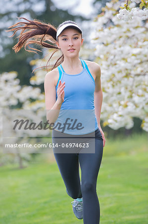 Teenage girl wearing blue sportswear running in park - Stock Photo