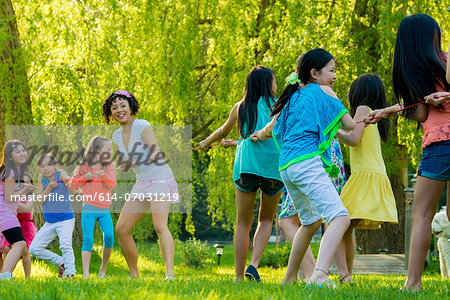 Woman and group of girls doing tug of war in park