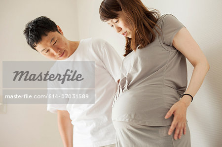 Man and pregnant woman looking down at stomach, portrait