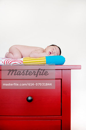 Baby boy sleeping on top of red drawers