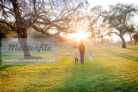 Father walking with son and daughter in sunlit field
