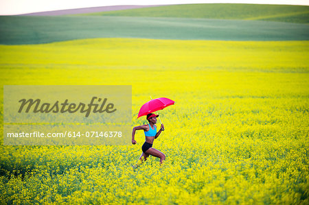 Young woman running in oil seed rape field with red umbrella Young woman running in oil seed rape field with red umbrella