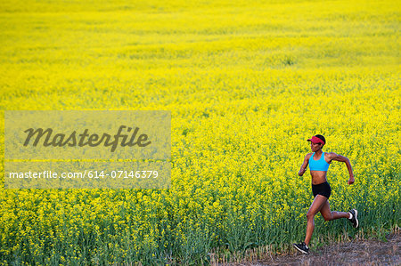 Young woman running next to oil seed rape field Young woman running next to oil seed rape field