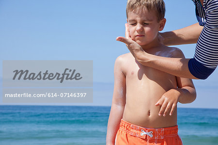Mother applying sun cream to sons face at beach