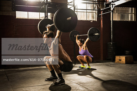 Two young adults lifting barbells in gym