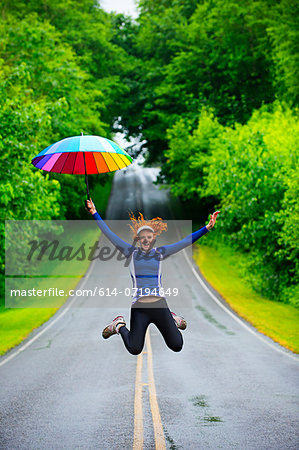 Teenage girl jumping with umbrella on road, Bainbridge Island, Washington, USA Teenage girl jumping with umbrella on road, Bainbridge Island, Washington, USA