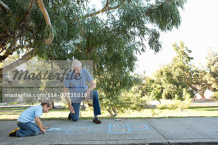 Grandfather and grandson drawing hopscotch