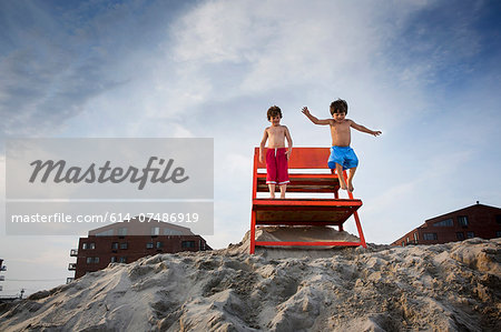 Two boys jumping off red notice board, Long Beach, New York State, USA