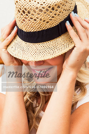 Young woman putting on straw hat Young woman putting on straw hat