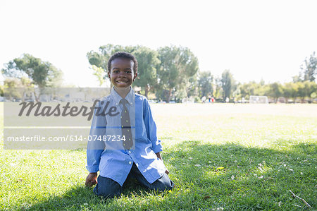 Portrait of boy kneeling on grass in sunlit park