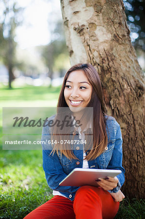 Young woman leaning against tree, using digital tablet