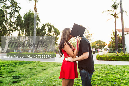 Couple kissing behind mortarboard
