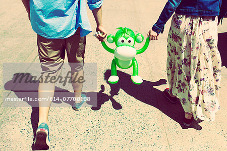 Cropped rear view of couple holding hands with inflatable monkey