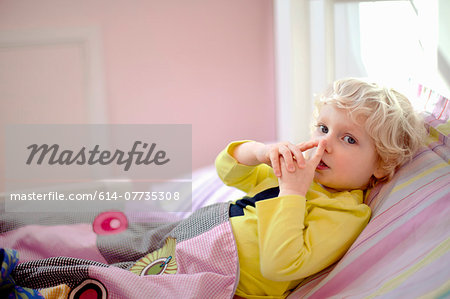 Male toddler lying in bed making secret hand gesture sign