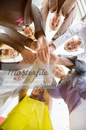 Worms eye view of seven business women and men in a circle holding hands in office