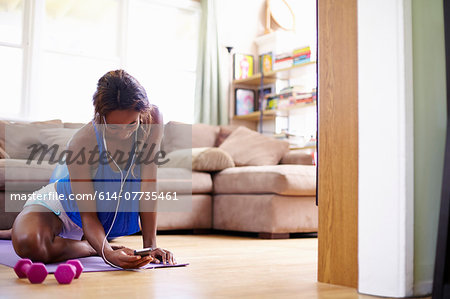 Young woman exercising on sitting room floor whilst looking at smartphone