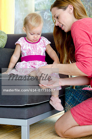 Mid adult mother putting on baby daughter's shoes