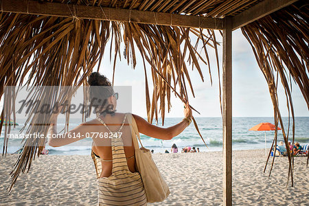 Young woman standing under cabana looking out to sea