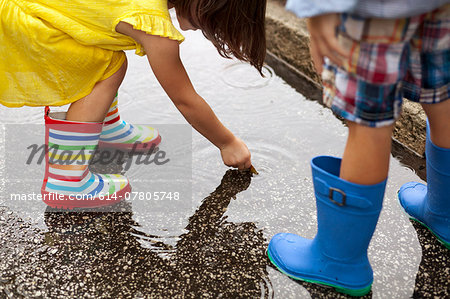 Boy and sister wearing rubber boots looking down at in rain puddle