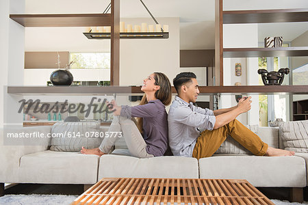 Couple sitting back to back playing games on smartphones on sitting room sofa