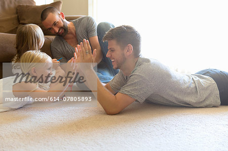 Male couple and two daughters playing clapping game on sitting room floor