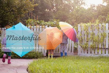 Boy and two sisters playing in garden carrying umbrellas
