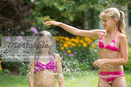 Girls in swimming costume playing with garden sprinkler Stock