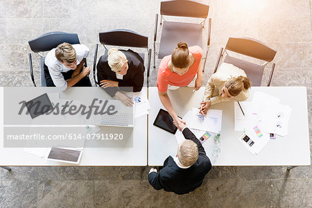 Overhead view of businessmen and women shaking hands with client at desk in office