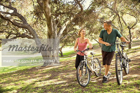 Mature couple chatting and pushing bicycles through park