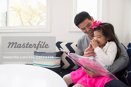 Mature man and daughter reading storybook on sofa