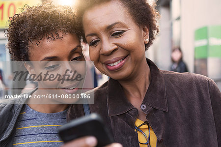 Close up of two mature female friends reading smartphone texts on street