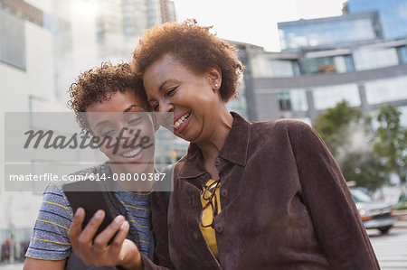 Two mature female friends laughing at smartphone texts on street