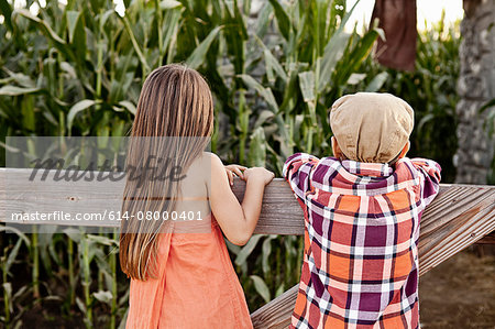 Rear view of boy and girl leaning against field fence