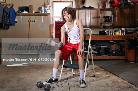 Slim boy struggling to lift hand weight in garage