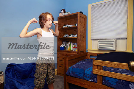 Slim boy flexing arm muscles in bedroom