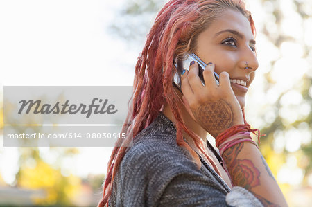Young woman with pink dreadlocks chatting on smartphone in park