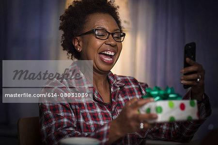 Mature woman holding gift taking selfie at home