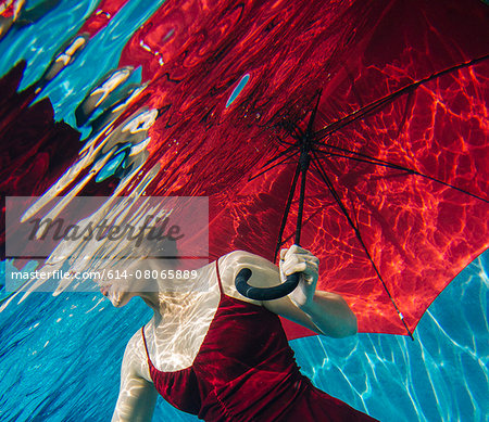 Mature woman wearing red dress, holding red umbrella, underwater view, mid section