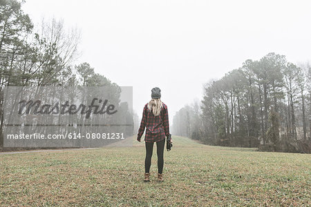 Rear view of young female photographer standing in misty field