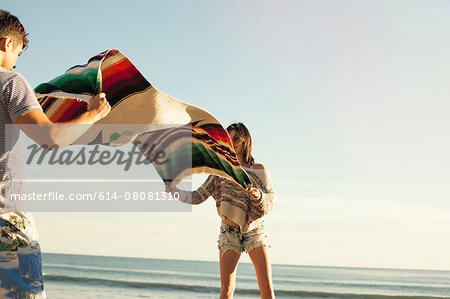 Young couple at beach, shaking out picnic blanket