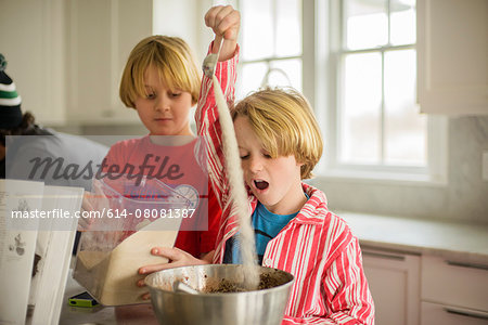 Brothers pouring flour into mixing bowl in kitchen