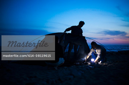 Group of friends setting up tent on beach at sunset